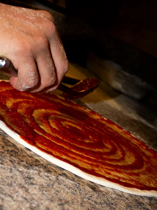 Una mano extiende el tomate en espiral con el cazo sobre la masa