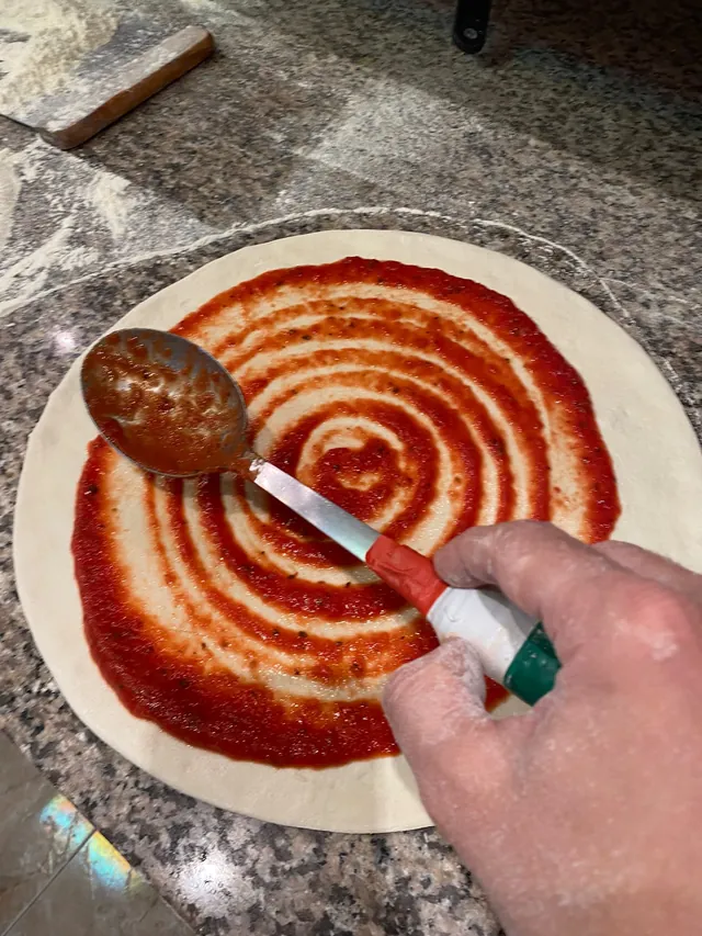 Una cuchara extiende el tomate en espiral sobre la masa